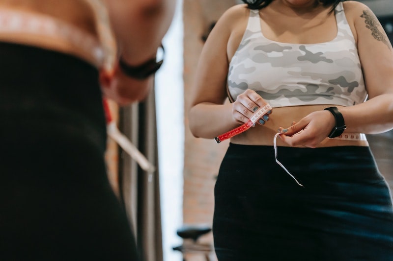 A woman measuring her waist, wearing gym clothes
